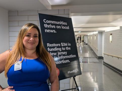 Free Press Action's Vanessa Maria Graber standing beside a sign at the New Jersey statehouse