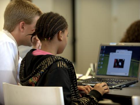 A photograph of a child typing on a computer next to a teacher